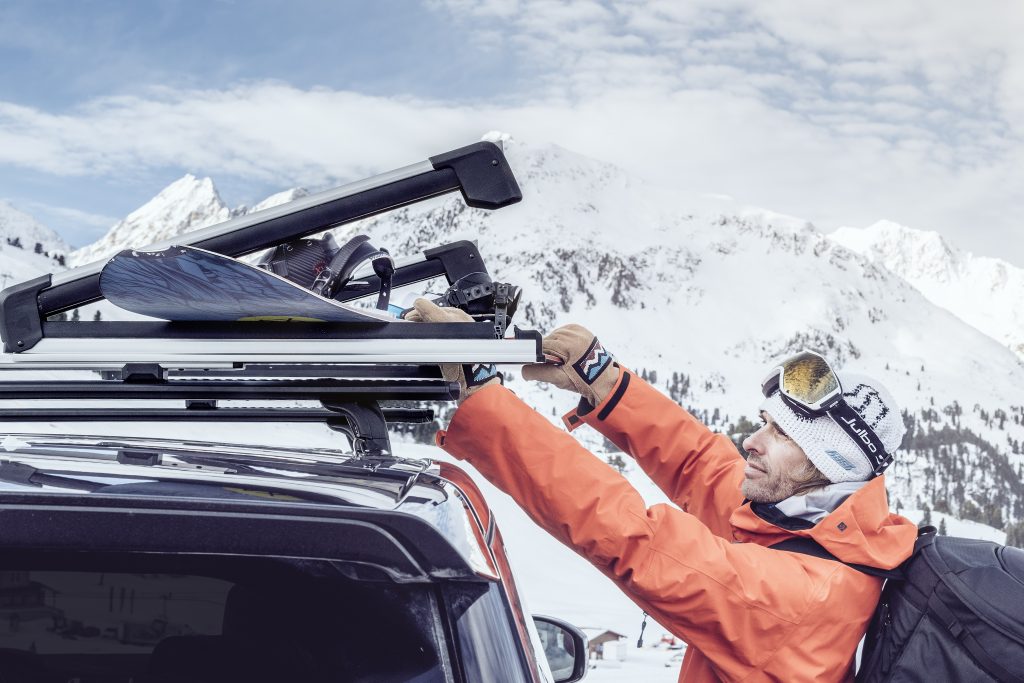 man installing snowboard into thule roof rack