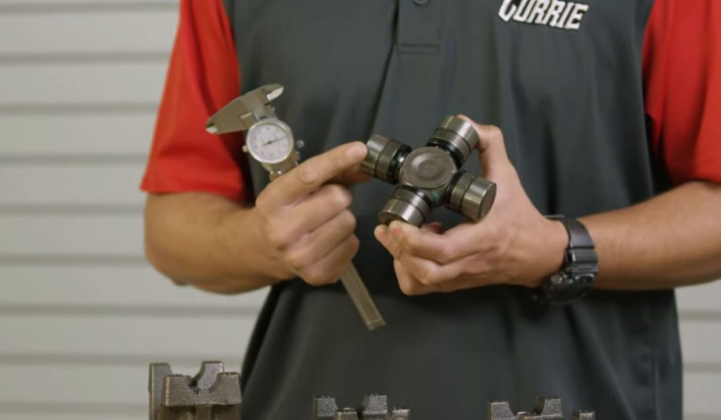 man holding a u joint and dial caliper to measure for the right driveshaft yoke