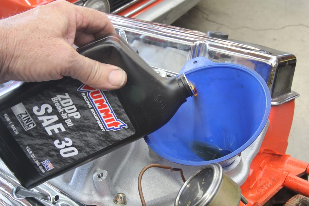 a man pours high zinc content zddp motor oil into a small block chevy engine prior to starting it for the first time