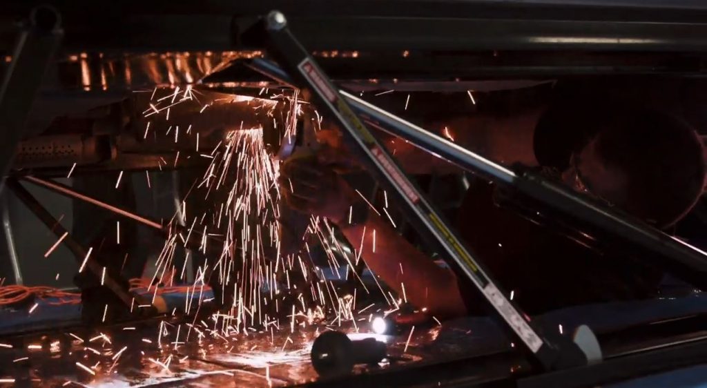 man grinding and cutting on a vehicle, with sparks flying