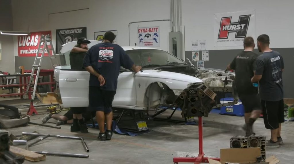 men working on building an sn95 ford mustang into a drag race car