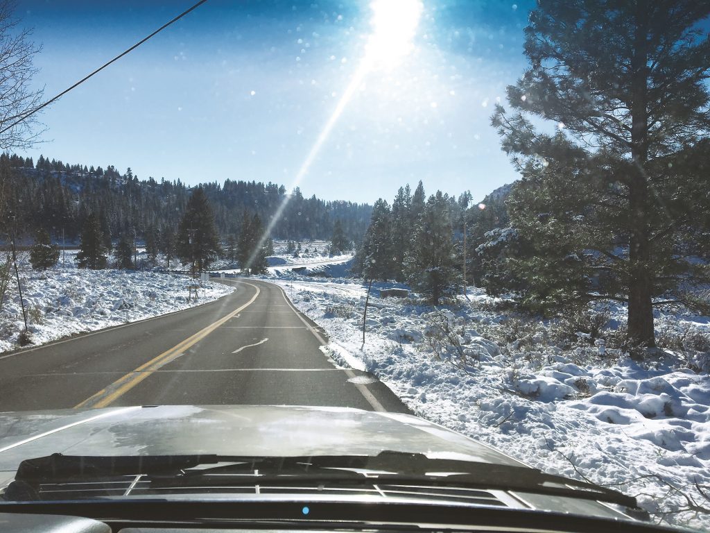 view of a pristine snow covered wooded mountain road from the passenger seat of a vehicle