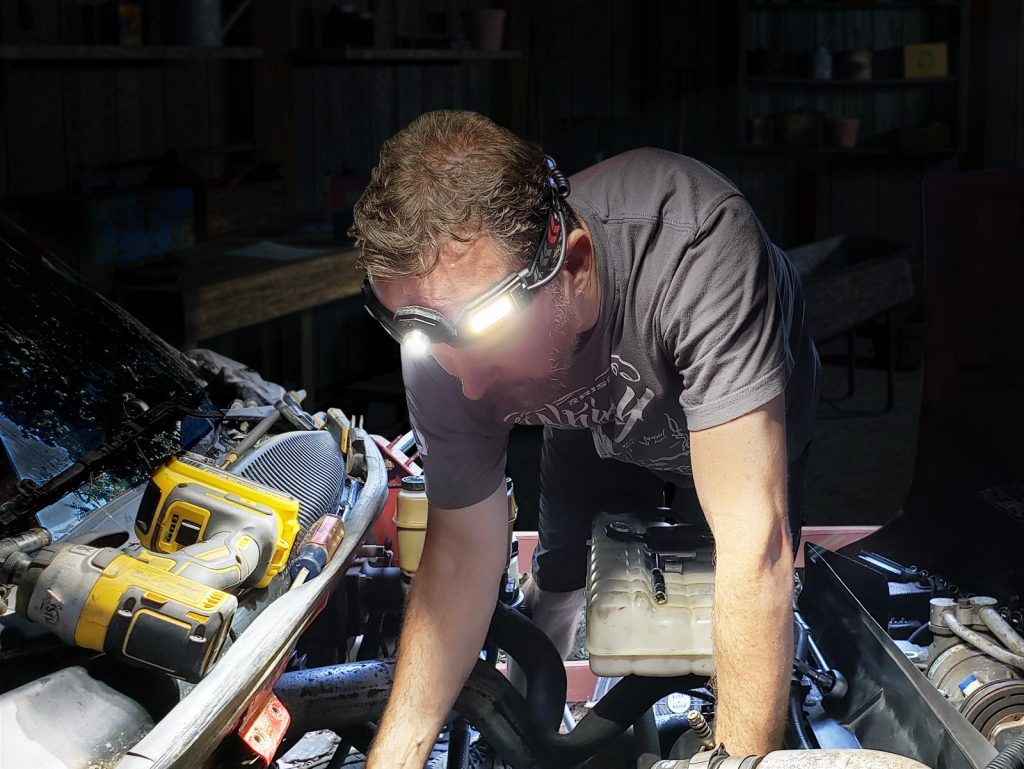man working on engine at night with a forehead-mounted flashlight