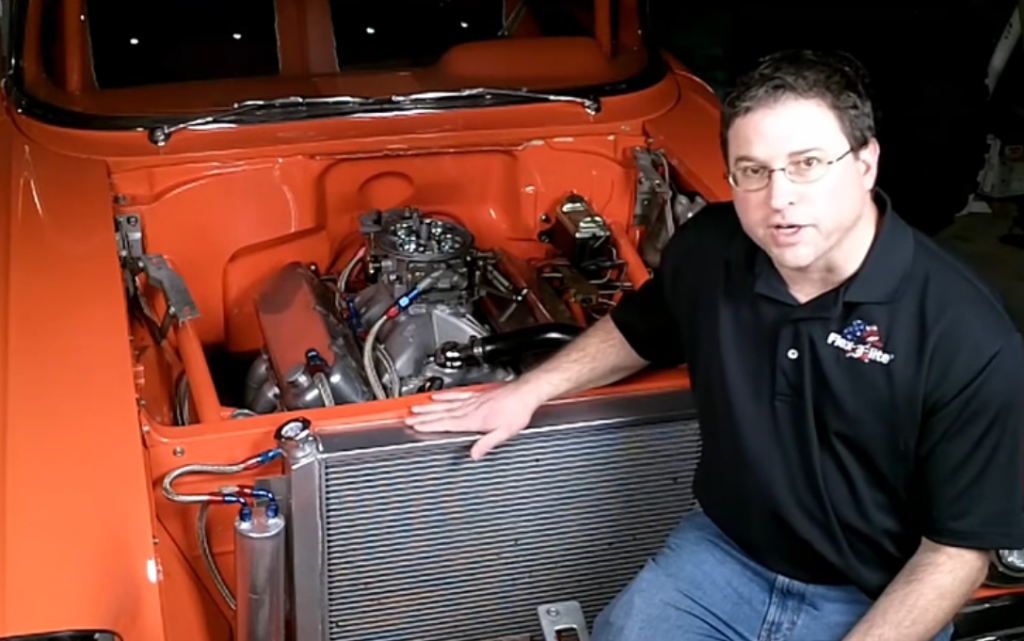 man sits on bumper of bel air chevy to do a radiator cooling system test