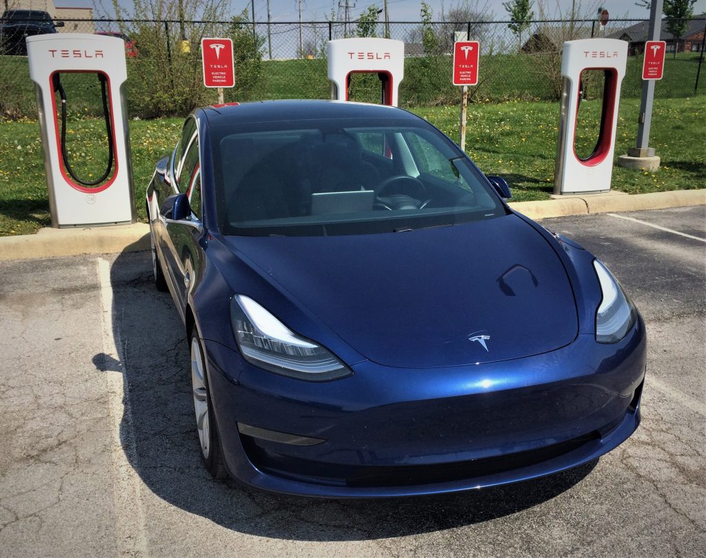 blue tesla model 3 charging at a supercharger station