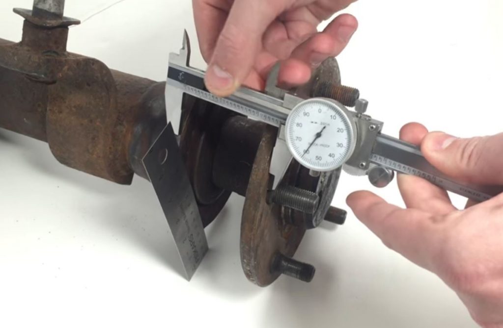 man measuring brake standoff from axle flange with a dial caliper