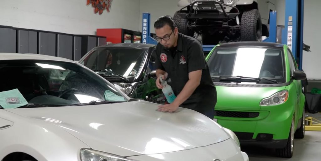 man wiping detailing spray from the hood of a white toyota 86 sports car