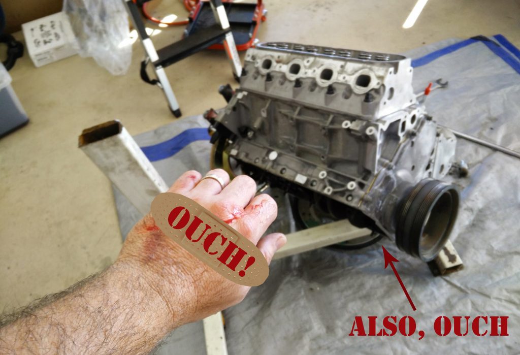 man wiht bandaged hand in front of a broken engine stand and engine laying on concrete floor