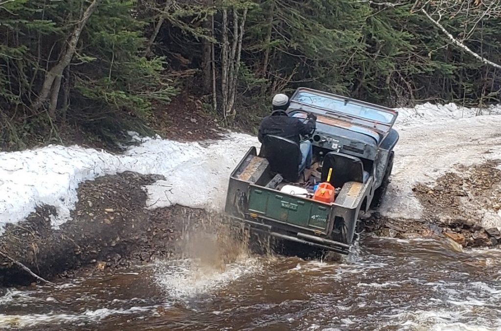 vintage willys jeep cj-2a fording river on snowy mountain trail