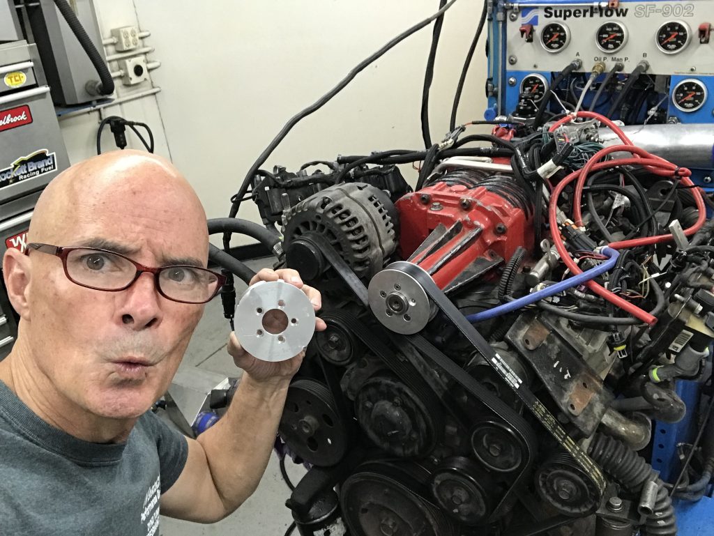 rcihard holdener holding a supercharger pulley in front of a pontiac 3800 v6 on an enigne dyno