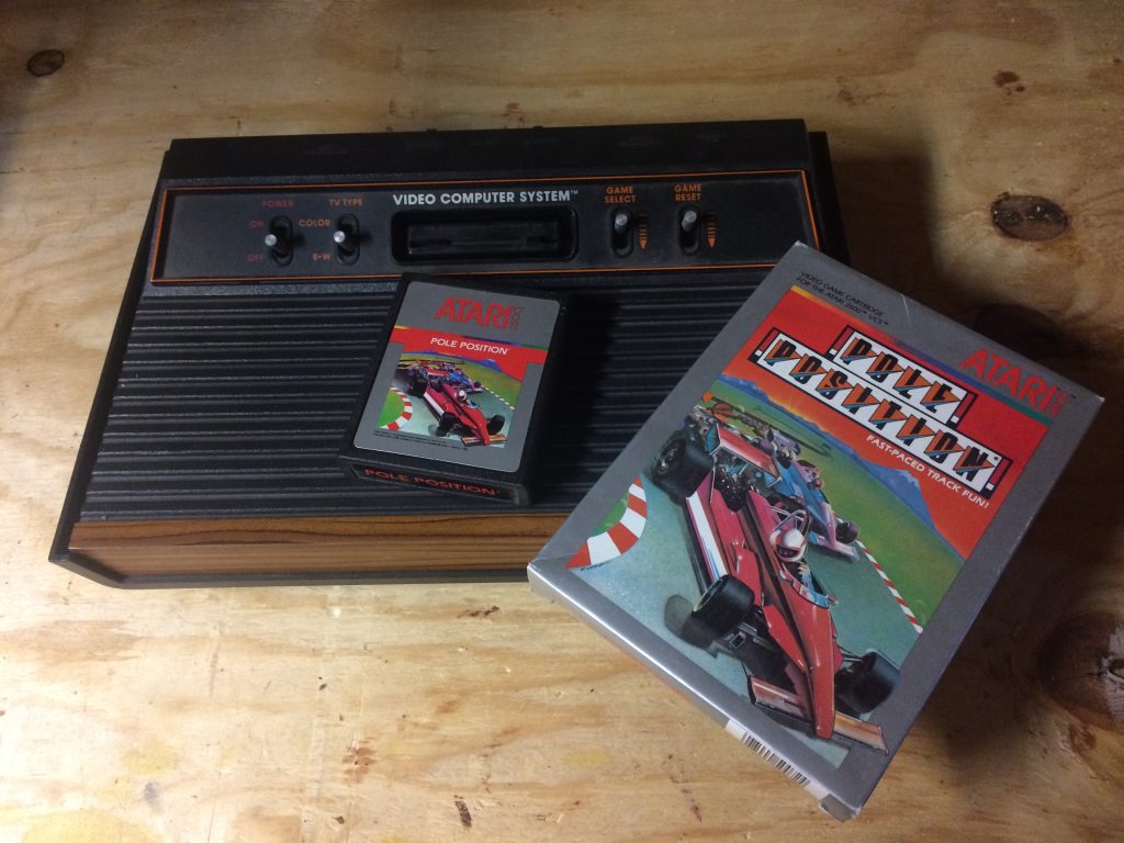 atari 2600 video game console sitting on a wood table with a pole position race car game cartridge
