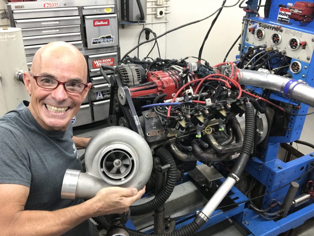 Richard holdener with a large turbocharger in front of a supercharged pontiac 3800 on an engine dyno