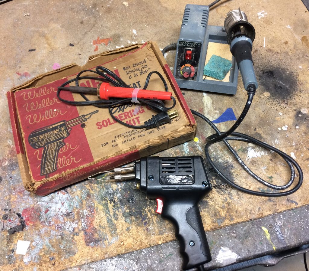 collection of soldering tools, guns, and irons on workbench
