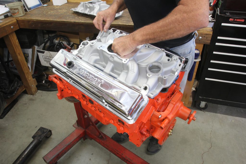 man placing intake manifold on top of a small block chevy on on an engine stand