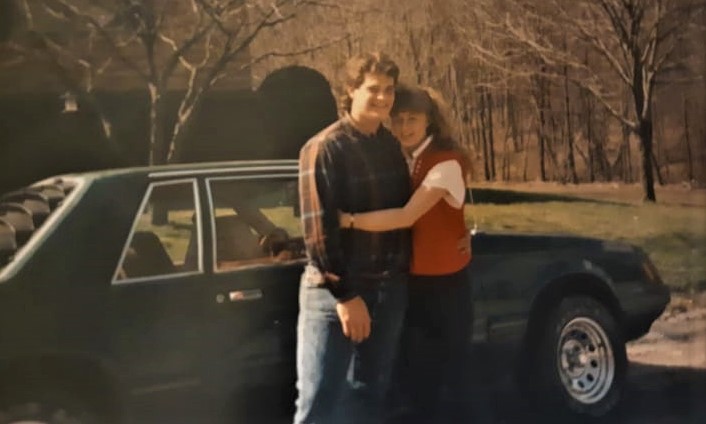 young couple post together in front of a fox body ford mustang in vintage photograph