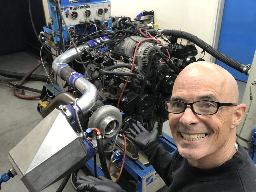 richard holdener poses in front of engine dyno with supercharged and turbocharged pontiac buick 3800 engine