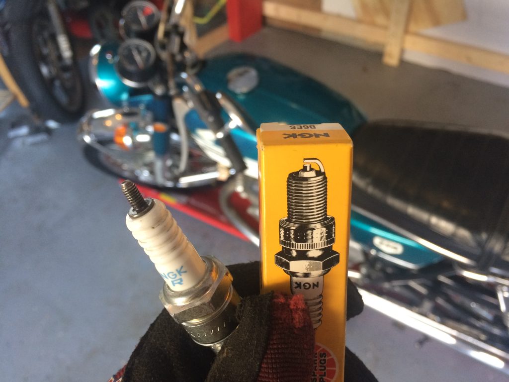 pair of spark plugs being held up in front of a 1970 honda cb350 motorcycle