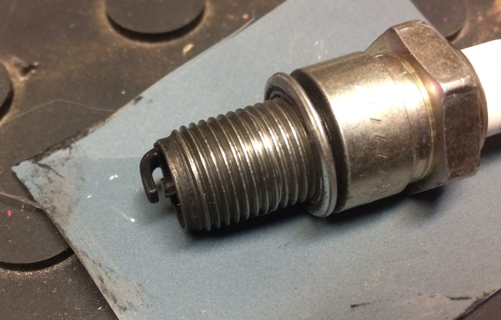 close up look at cleaning a spark plug electrode tip with fine grit sandpaper