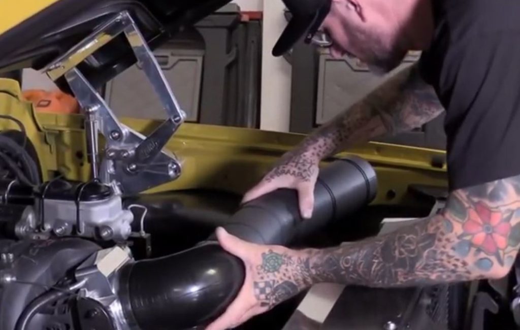 man installing a custom cut section of air intake tubing for an ls swapped vintage muscle car