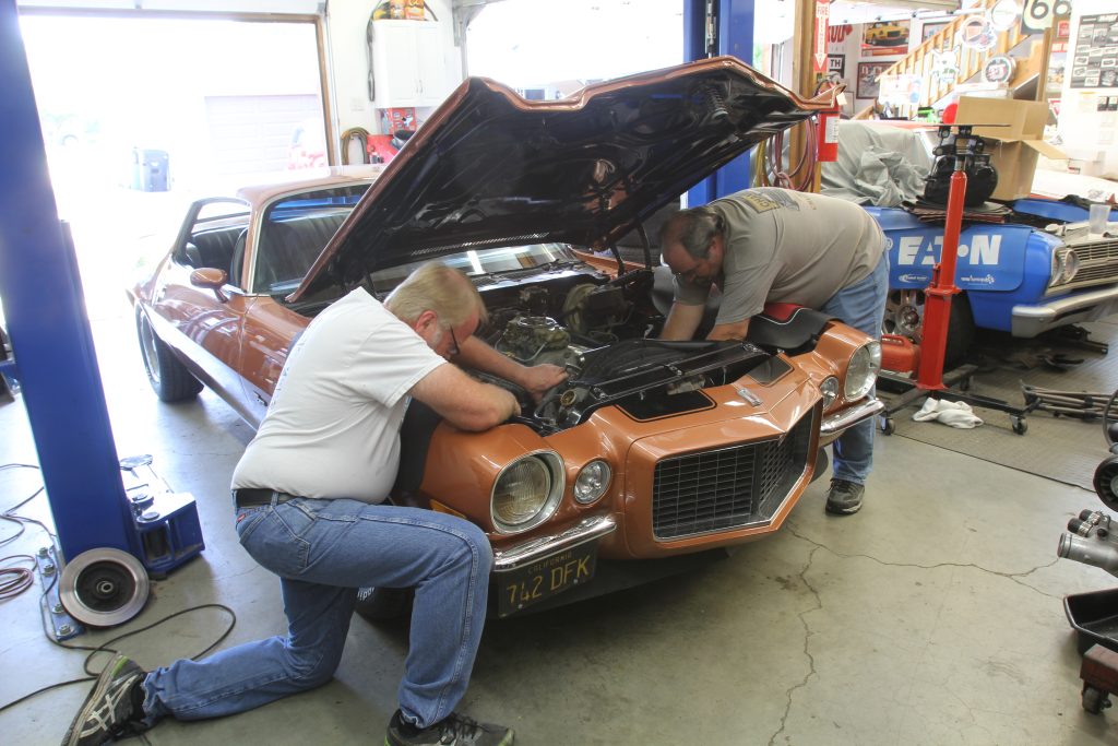 2 men working on second generation split bumper chevy camaro in auto shop garage