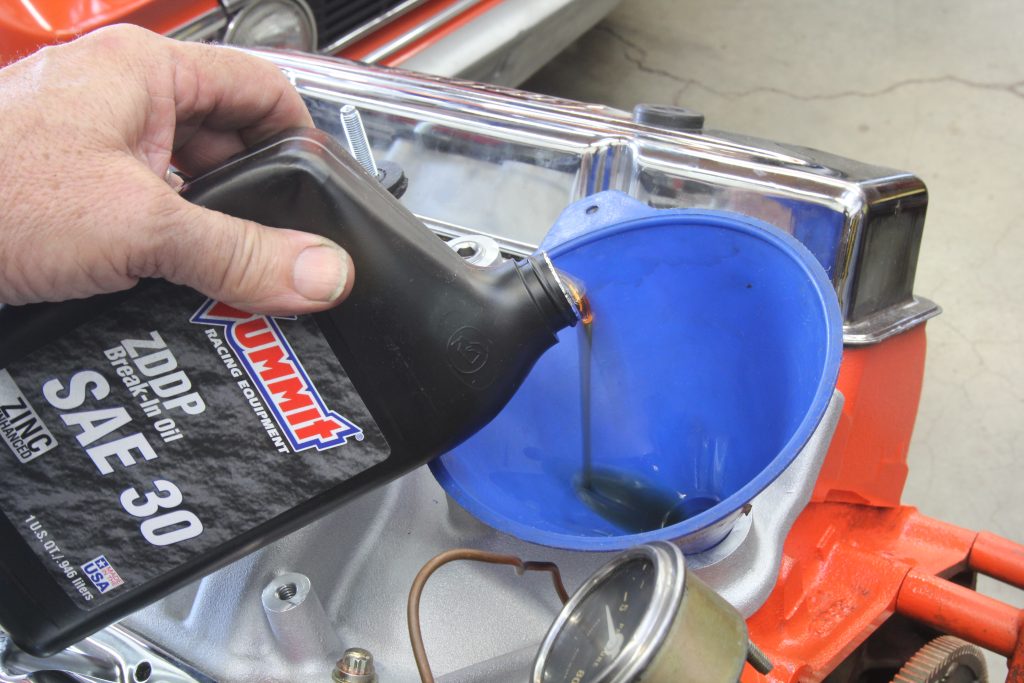man pouring summit racing high zinc break in motor oil into small block chevy v8 engine