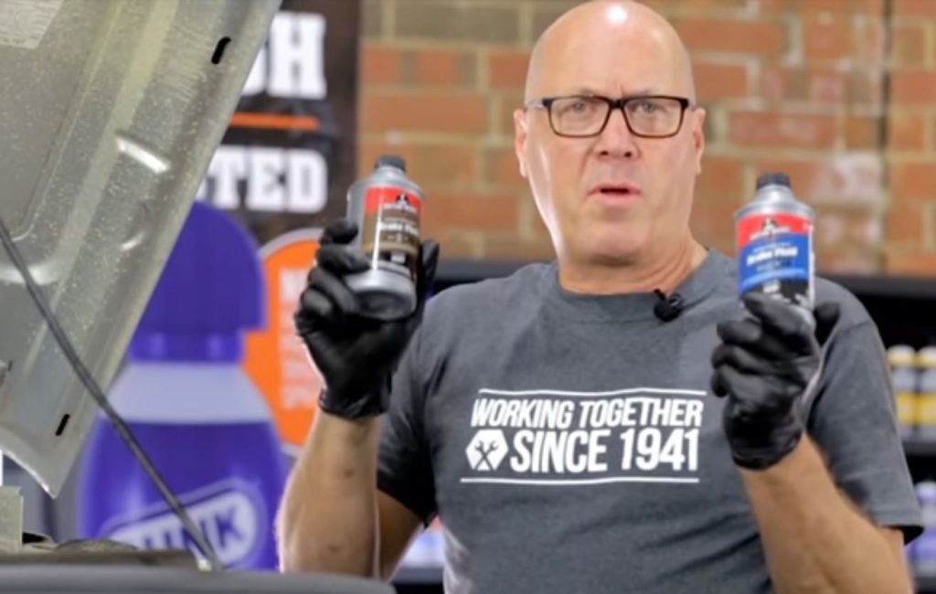 man holding a can of dot 3 and dot 4 brake fluid for side by side comparison