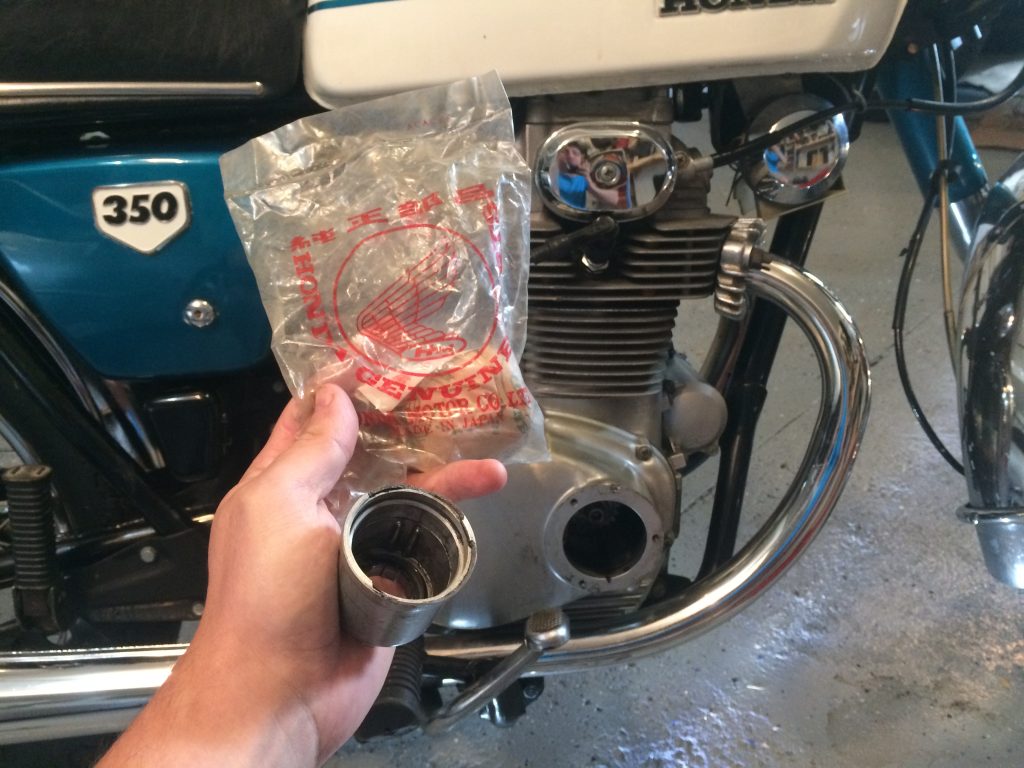 man holding a NOS bag and a damaged oil filter cup in front of a 1970 honda cb350 vintage motorcycle