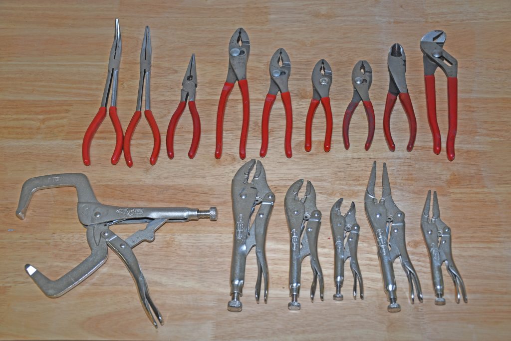 large group of pliers, locking pliers, needle nose and vise grips on workbench