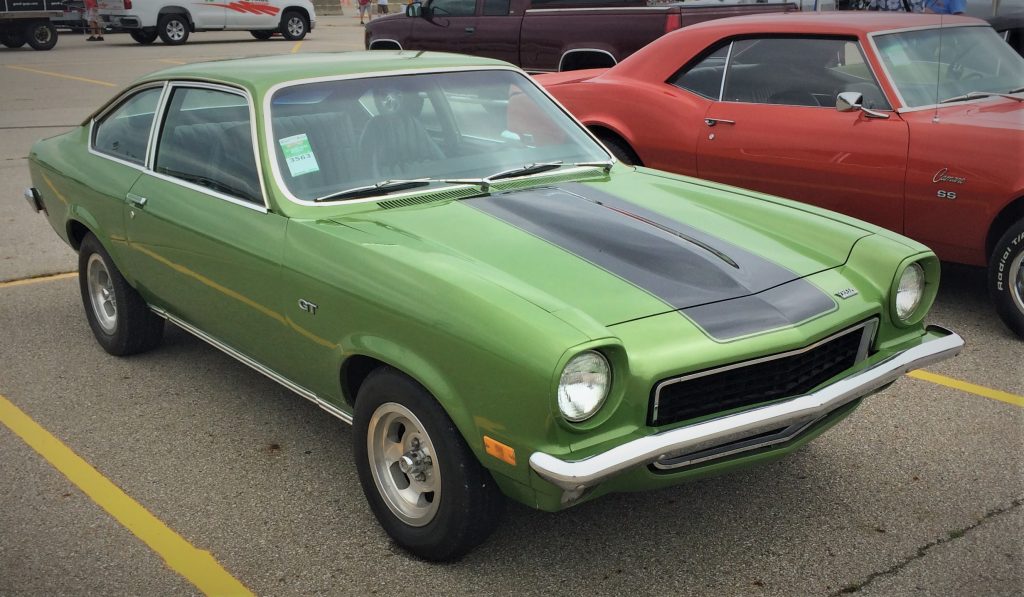 a green chevy vega with a black hood stripe at a classic car show