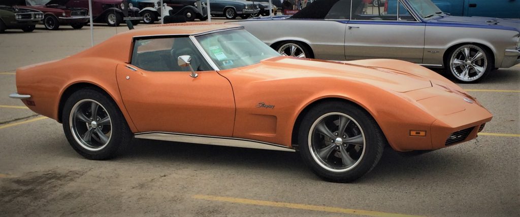 side view of an orange 1973 chevy corvette with custom wheels
