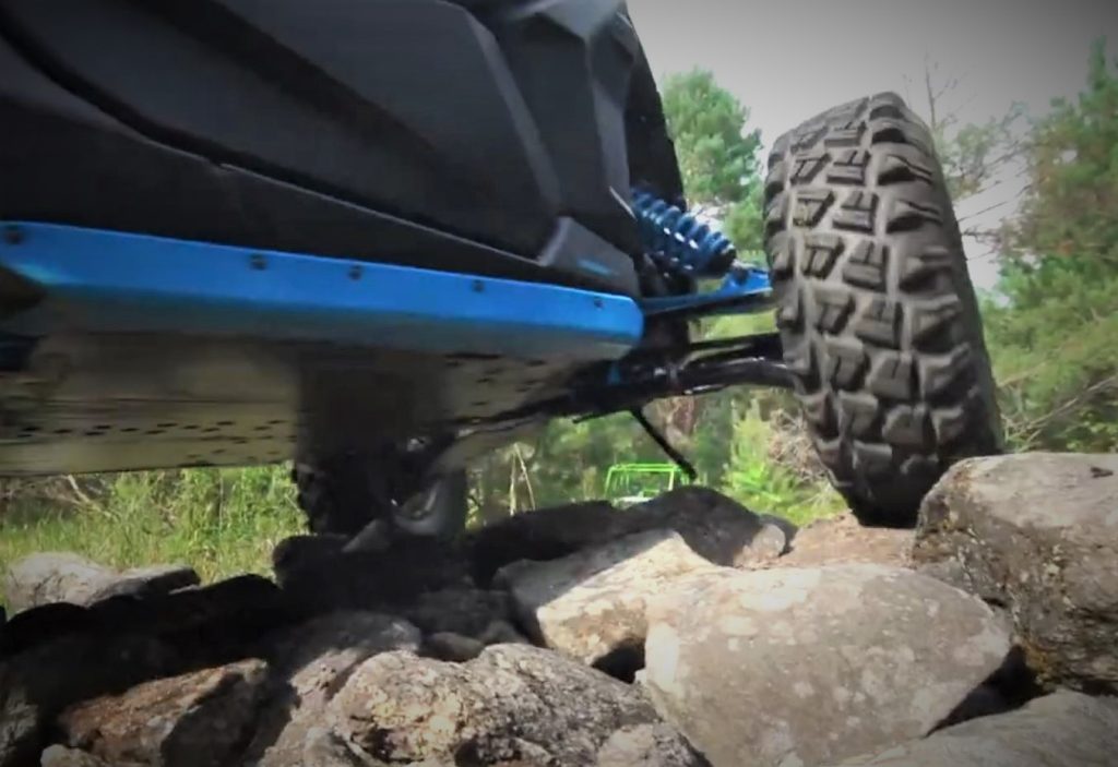 a low underside picture of a side by side off road powersports vehicle climbing over rocks with knobby tire