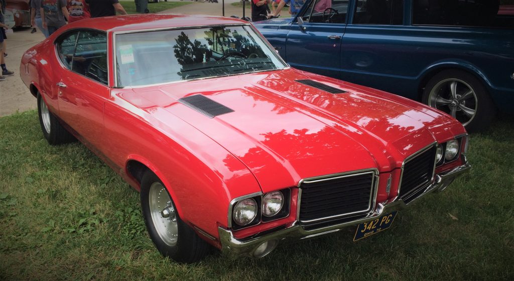 a red 1972 oldsmobile cutlass fastback coupe parked on grass at a classic car show