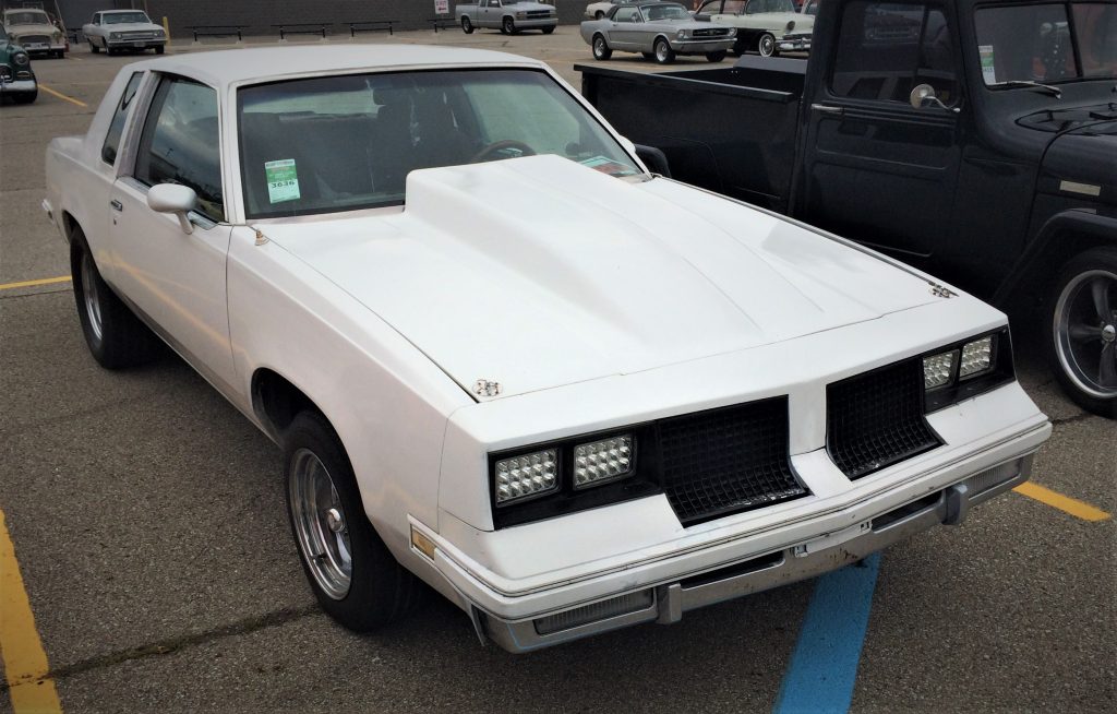 whgite 1987 oldmsobile cutlass parked at a car show