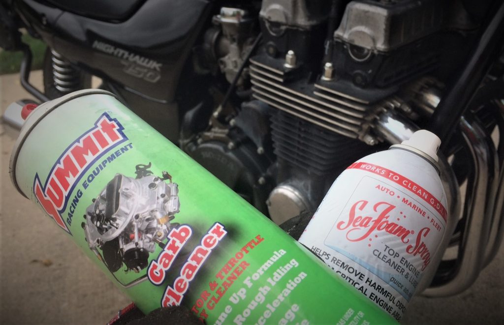 a can of seafoam and carburetor cleaner held in front of a motorcycle