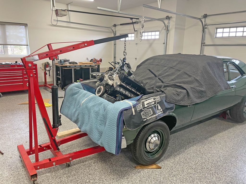 engine being lowered into a vintage chevy nova muscle car