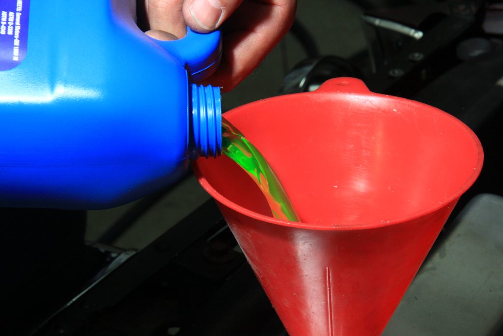 pouring engine coolant into a radiator from a jug and funnel