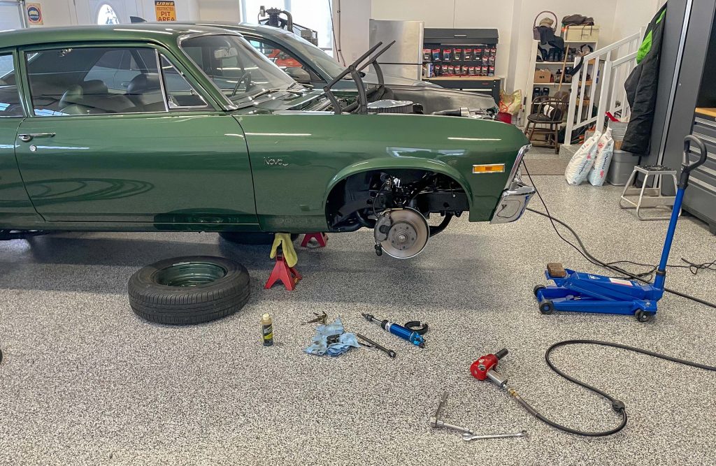 vintage green chevy nova in garage with wheel and tire removed for service