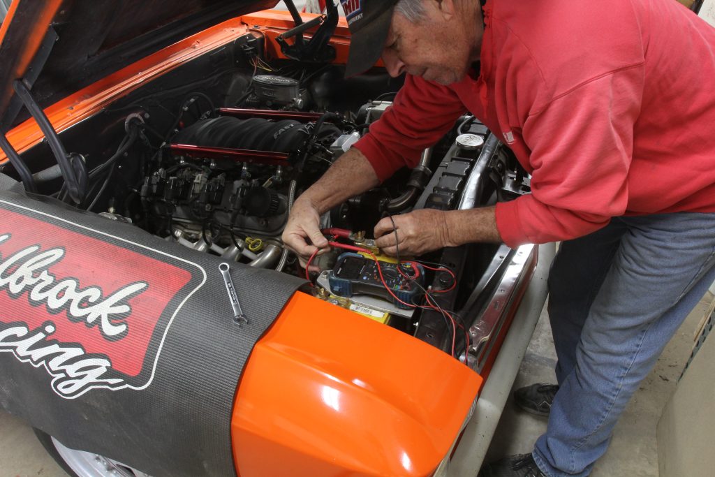 Man testing a vehicle battery in a classic car with a multimeter