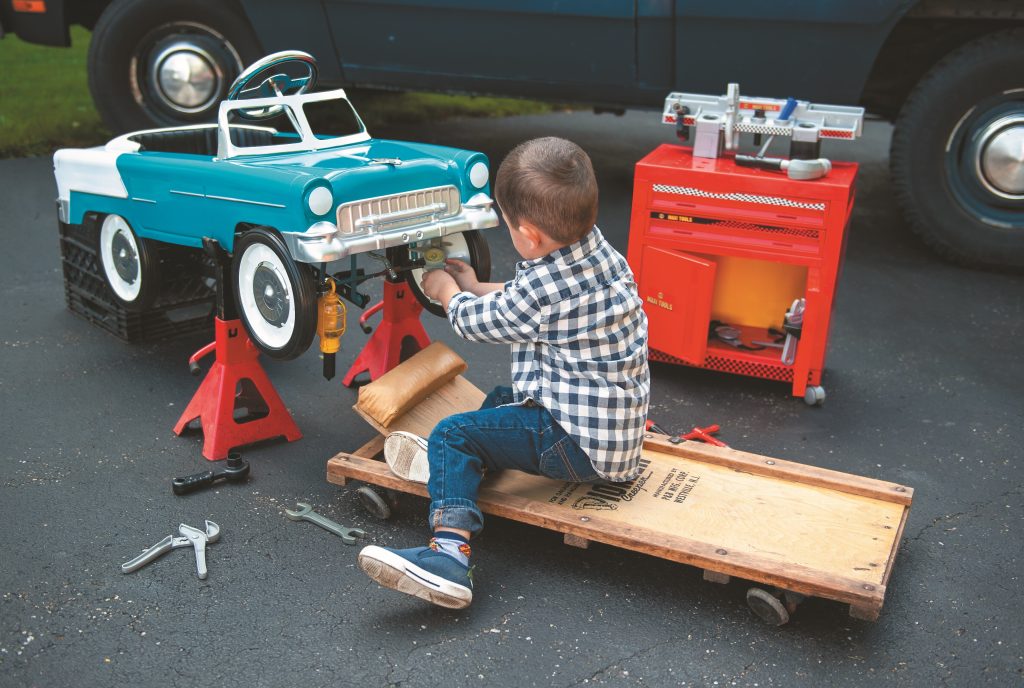 Young Boy working on a 1955 chevy pedal car in a driveway