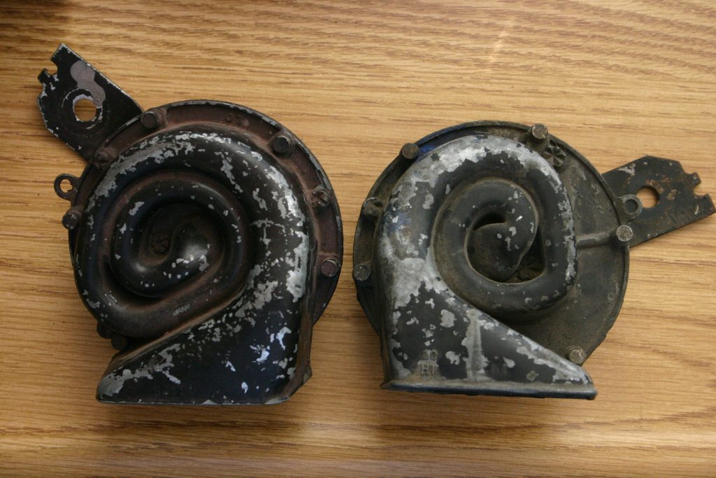 a pair of crusty old car horns on a workbench