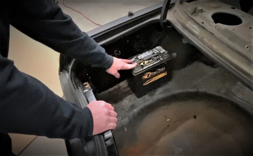 man pointing to a battery in the trunk of a project car