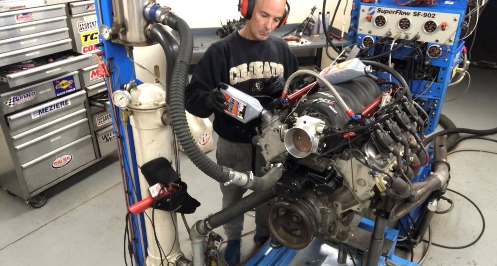 man pouring oil into an engine on a dyno