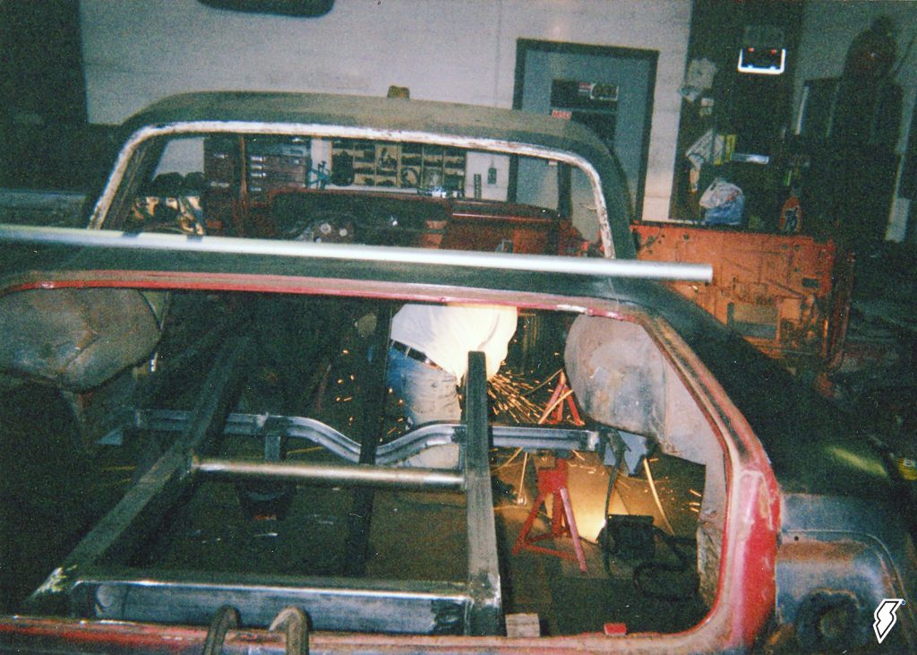 man welding chassis inside a 1962 impala race car
