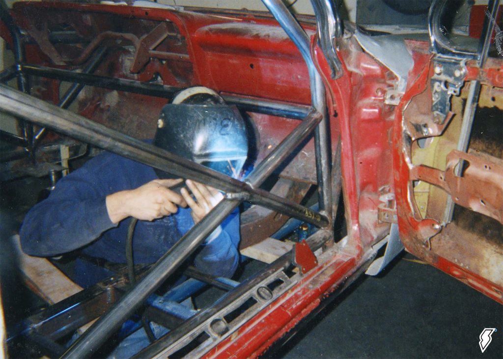 man welding roll cage into a vintage race car