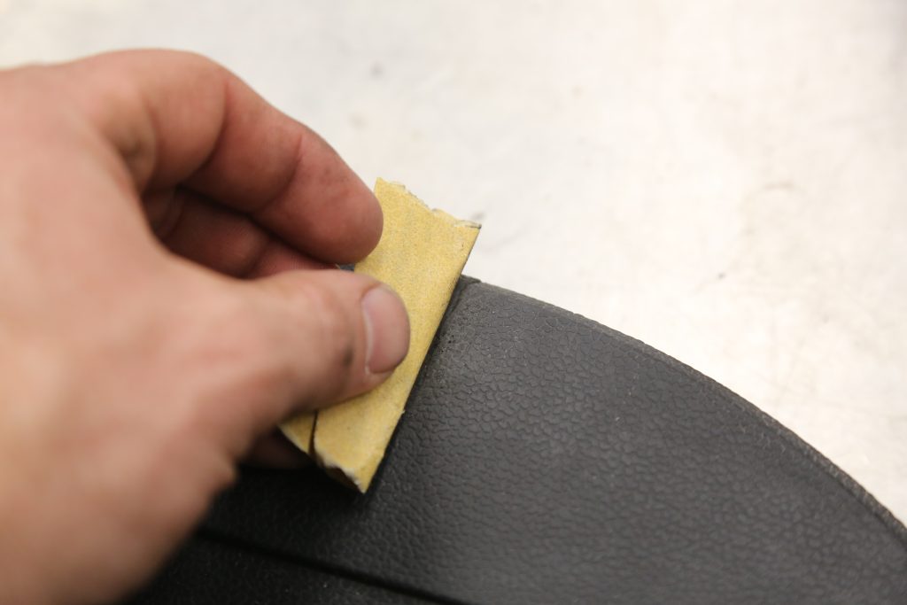 using fine grit sandpaper on a piece of automotive plastic