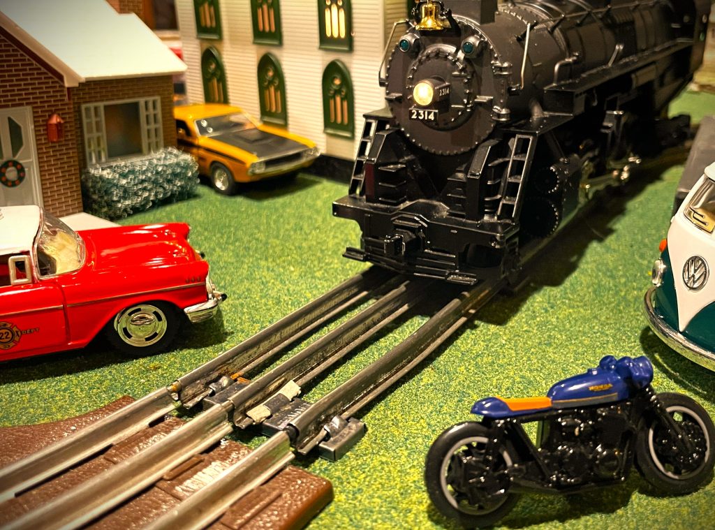 model train diorama scene with steam engine, old cars & motorcycle