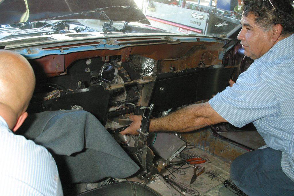 Men removing dash panel from a vintage ford mustang