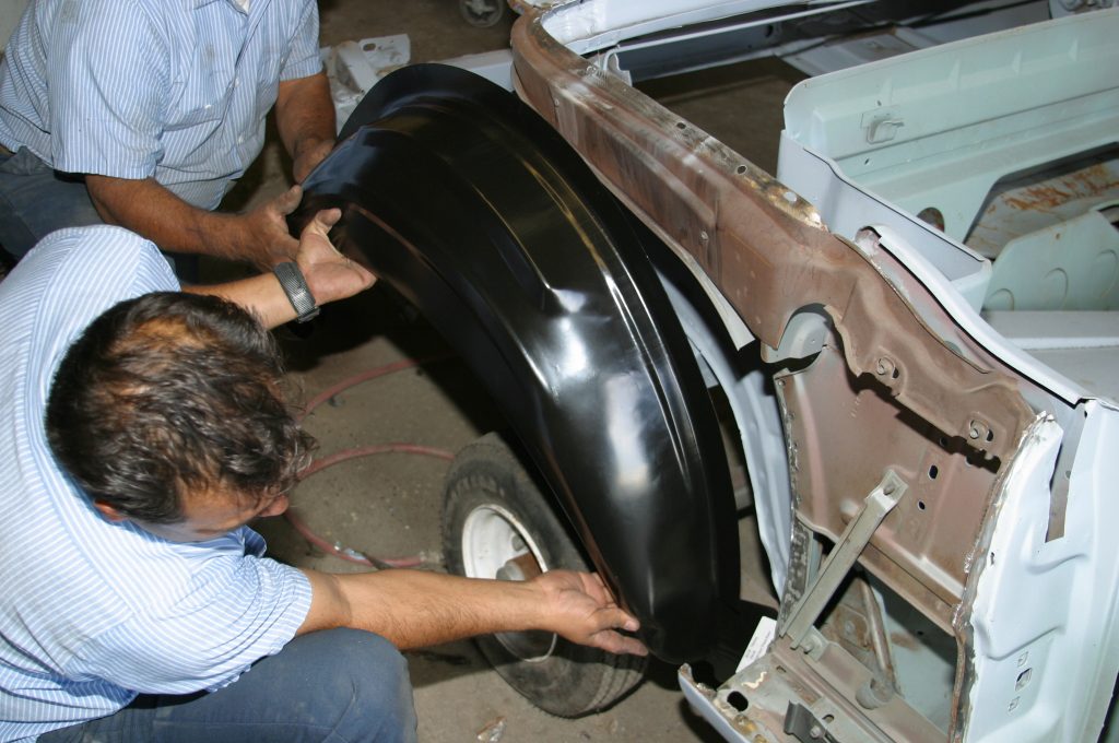man fitting a replacement inner fender into a car body