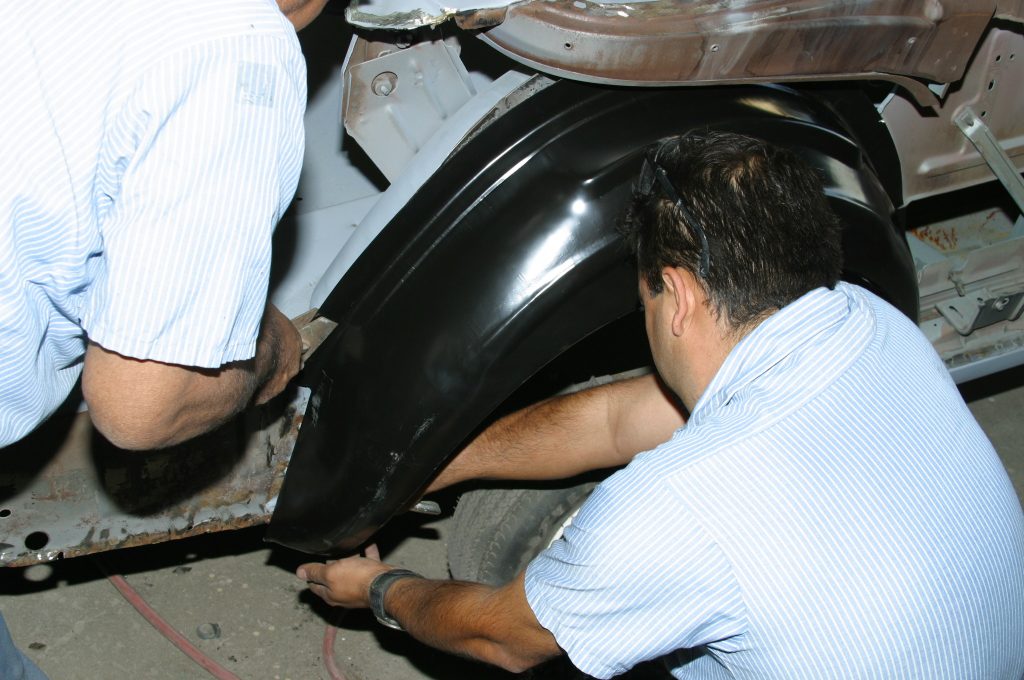 men fitting a fender liner into an old car body