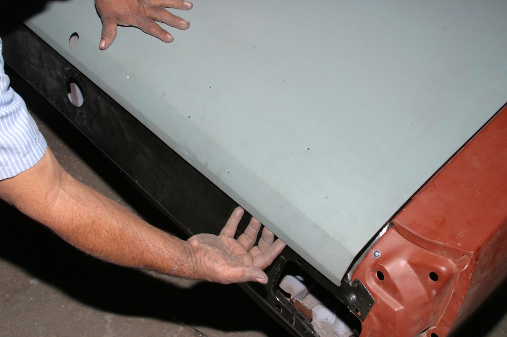 man fitting a sheetmetal panel to a car body